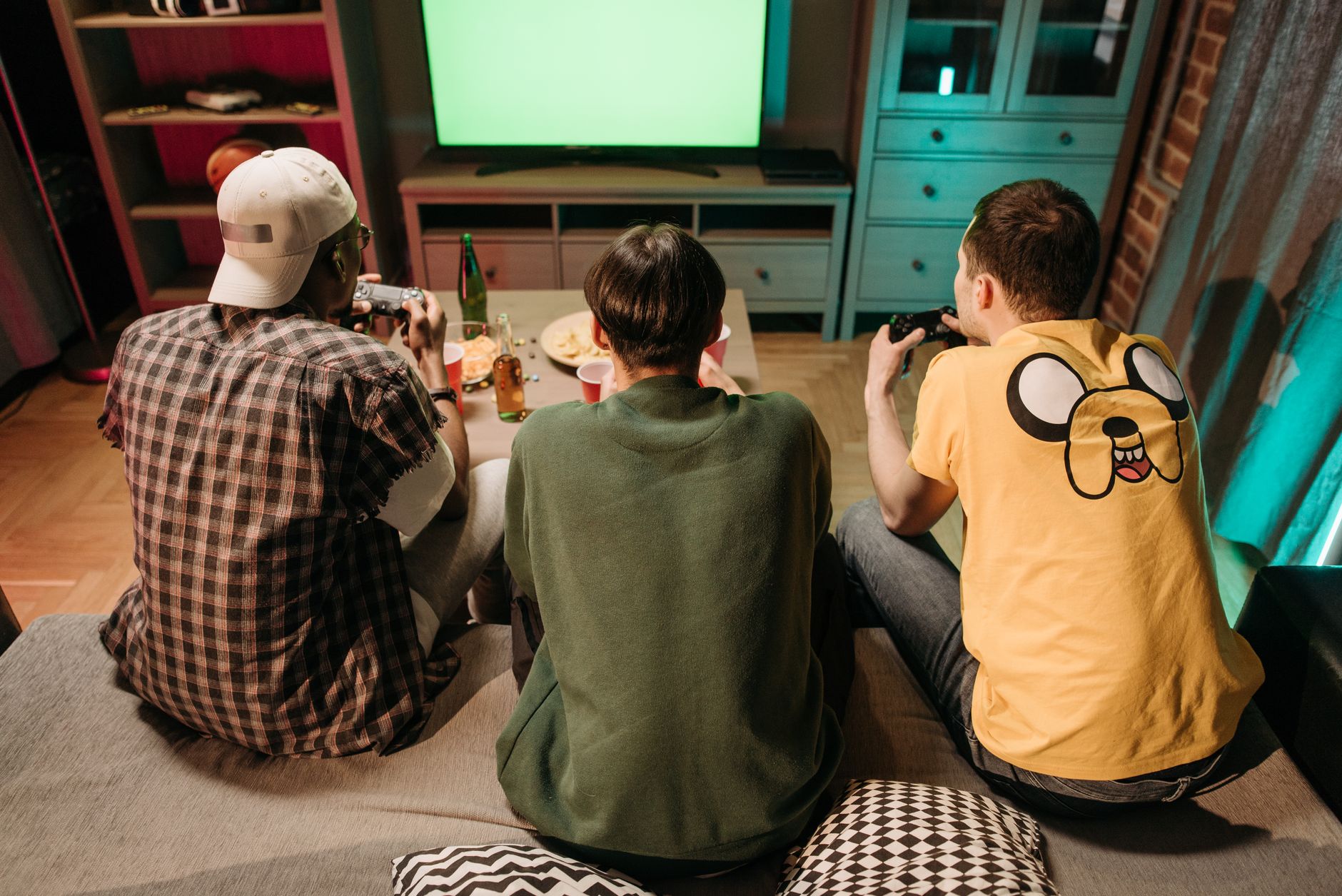 Three young men enjoying a home gaming session together, playing video games in a cozy indoors setting. — A World of Slot Adv