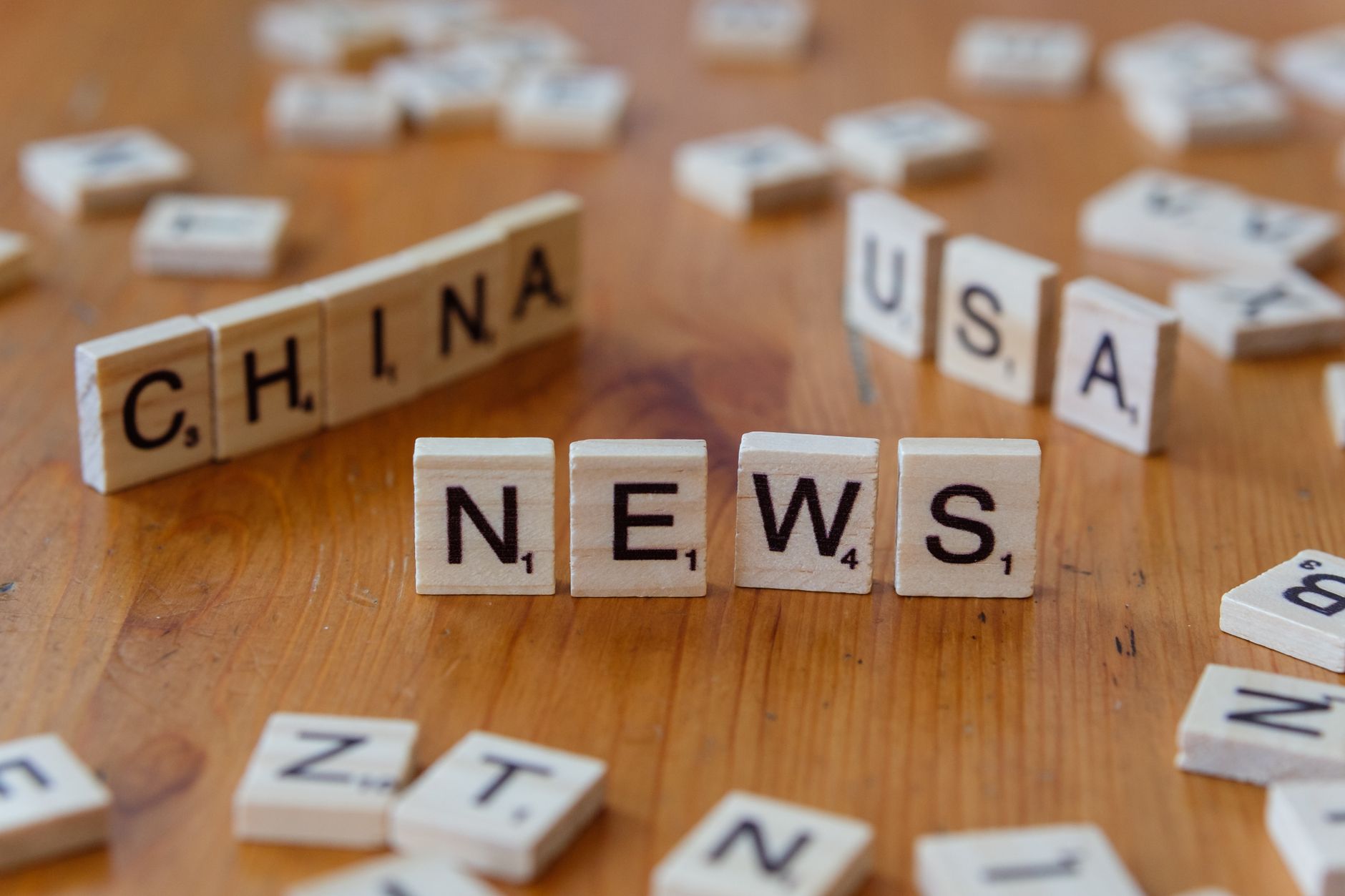 Wooden Scrabble tiles spelling 'NEWS' with 'CHINA' and 'USA' on a wooden surface. — Baccarat: The Classic Card Game That Comb