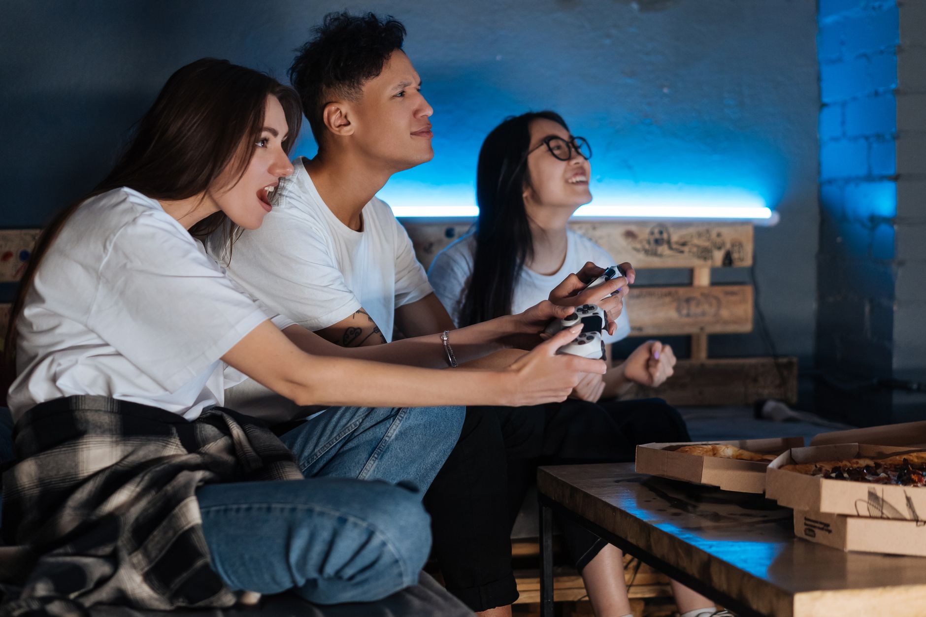 Three friends play video games together indoors, enjoying pizza and fun times. — Get Access to Axio88 with the Latest Officia