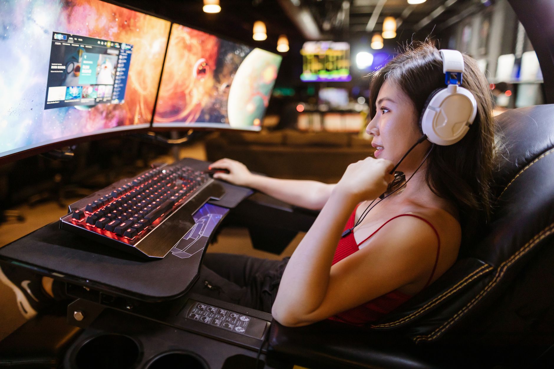 Young woman in red top gaming on dual monitors with white headphones in a modern setup. — Join PG88 for Seamless Betting Acro