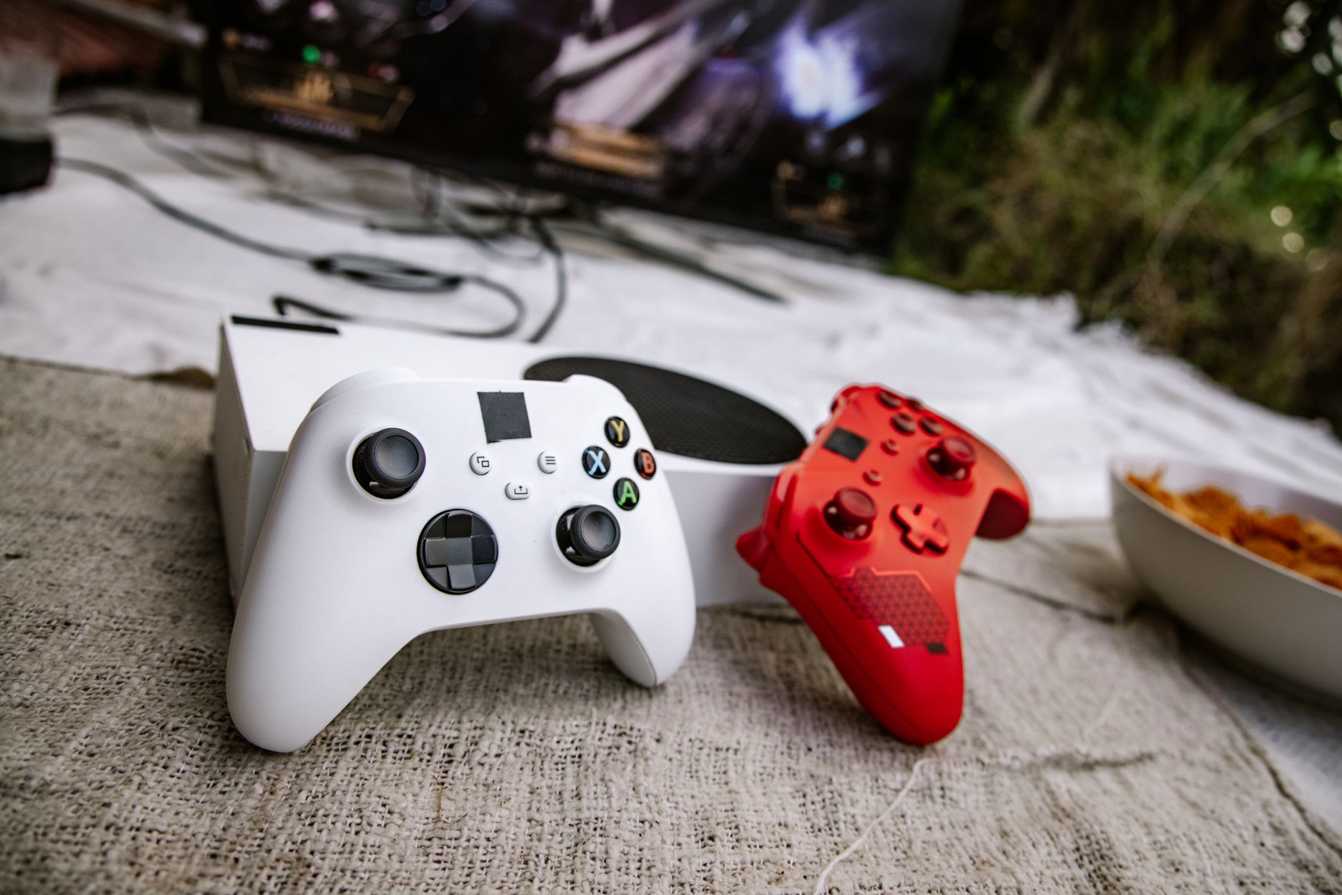White and red wireless gaming controllers on a textured surface near chips and a TV screen. — Play smarter with the seamless