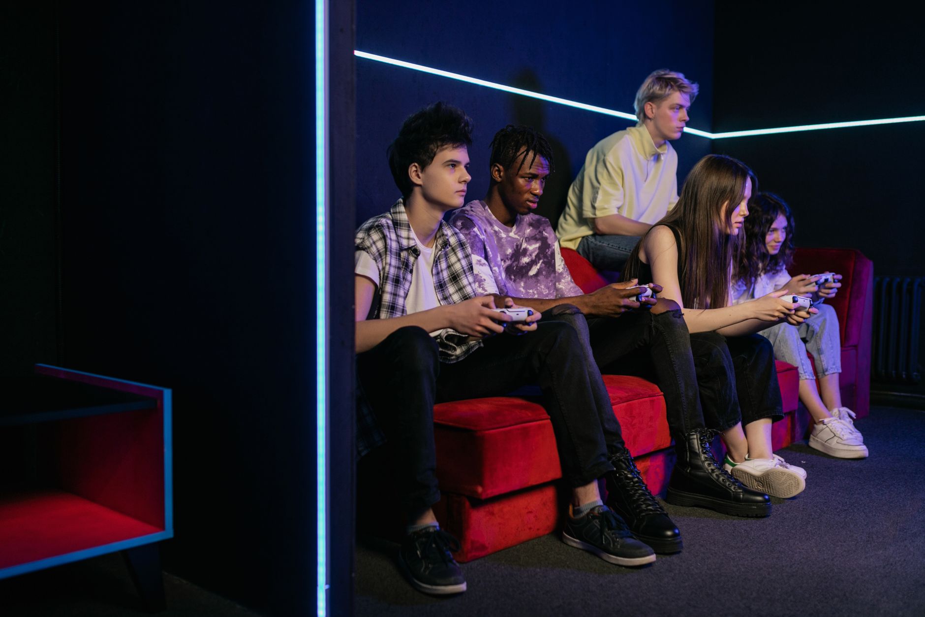 Teenagers enjoying video games together on a vibrant red couch in a modern gaming room. — Top Casino Games on Takabet, Brazin