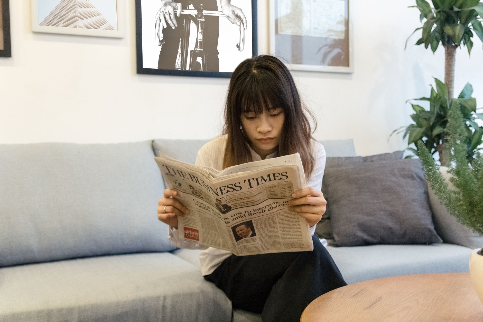 A young woman attentively reads a newspaper while sitting on a modern sofa indoors. — Toto TV Enhancing Sports Enjoyment With