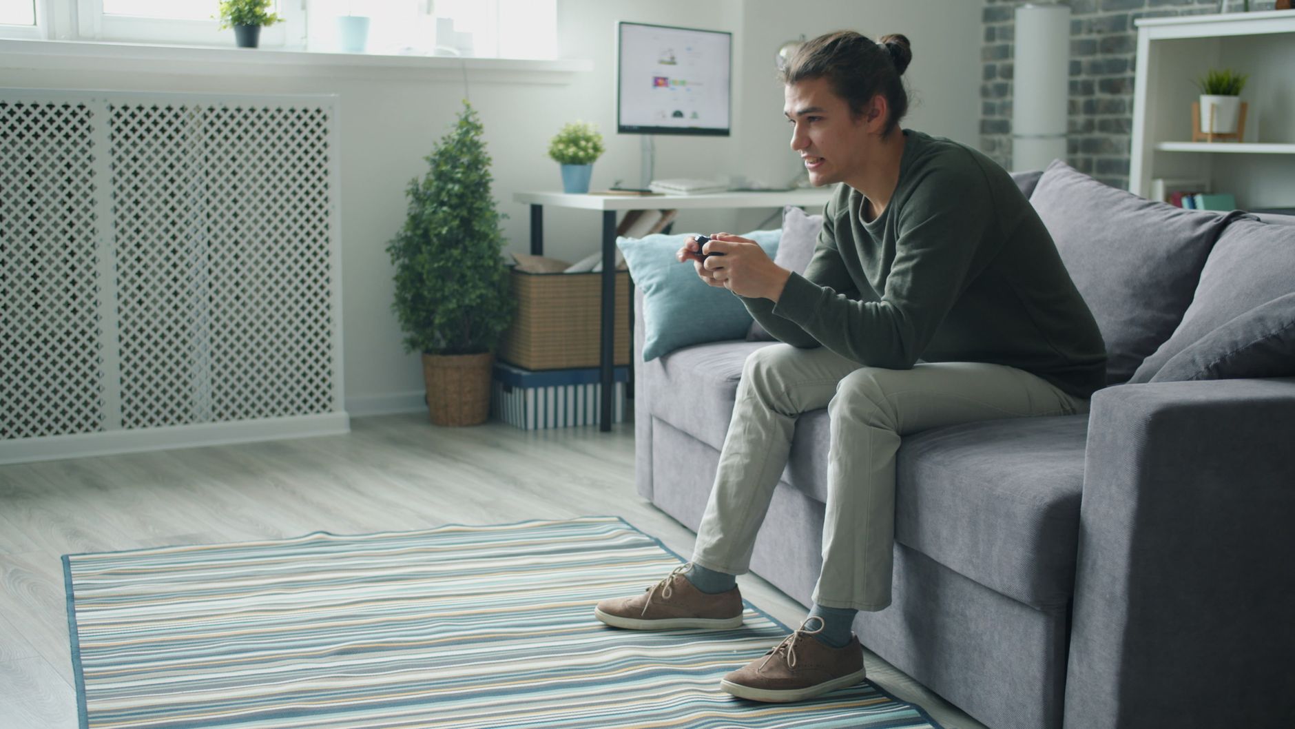 Smiling young man enjoying video games on a sofa at home. — Use Pasarbola for Convenient Online Gambling Anytime, Anywhere